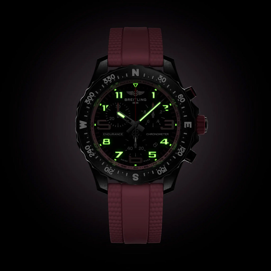 The BREITLING Endurance Pro 38 features a dark theme with glowing green numerals and hands, a round black dial, deep red textured strap, and durable Breitlight® case. Directional indicators embellish the bezel, while "Breitling Endurance Pro" is inscribed on the dial.